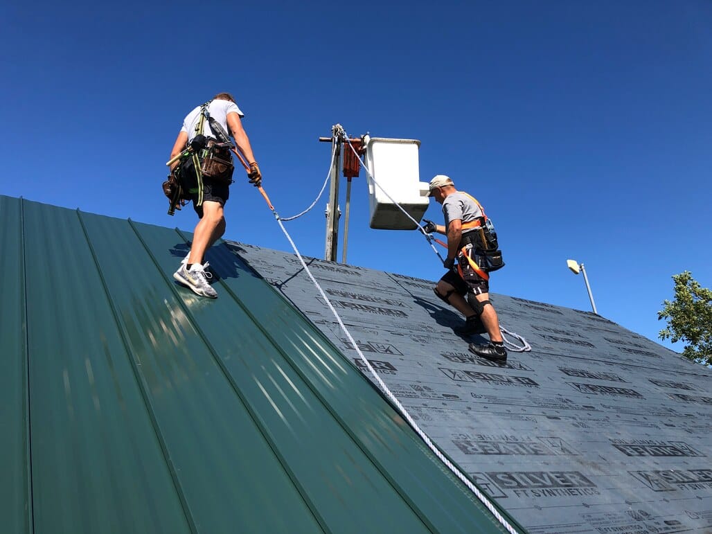 Roofing crew installing sheet steel roofing panels on commercial building